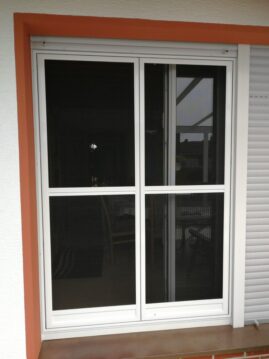 Fenster mit einem Insektenschutzgitter aus schwarzem Netz und weißen Rahmen.