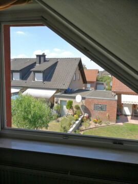 Blick durch ein Fenster auf benachbarte Häuser mit Gärten und einem Satellitenschüssel.