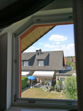 Blick durch ein Fenster auf ein Wohnhaus mit einem Garten und einer Terrasse.