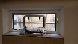 Ein Bullauge in einem Fenster mit einem schmutzigen Glas und einem Sichtschutz.