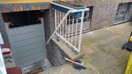 Graue Zugangstür mit einer Treppe und einem Blumenkasten darüber, der an einem Geländer befestigt ist.