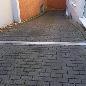 Ein horizontaler Metallbalken, der den Zugang zu einem gepflasterten Weg blockiert.