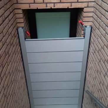 Graue Gartentür mit horizontalen Paneelen und Metallrahmen in einem Ziegelmauerwerk.
