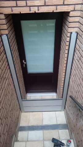 Eingangstür mit einem gläsernen Paneel und einem metallischen Rahmen in einem Mauerwerk.