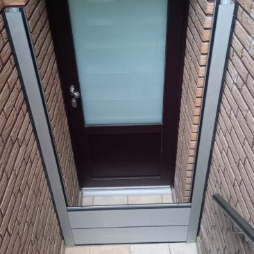 Eingangstür mit einem gläsernen Paneel und einem metallischen Rahmen in einem Mauerwerk.