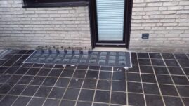 Kellerschachtabdeckung mit rechteckigen Glassteinen vor einem Fenster in einem Gebäude.