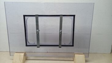 Transparente Wasserschott mit metallischen Halterungen auf Holzständern.