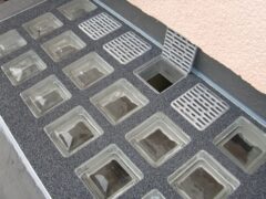 Glasabdeckungen für Lichtschächte in einem grauen Bodenbelag mit Abflussgitter.