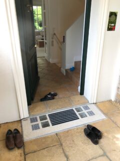 Eingangsbereich mit Schuhen und einer Lichtschachtabdeckung im Boden.