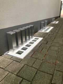 Aluminium Lichtschachtabdeckungen auf einem gepflasterten Boden in einer Reihe angeordnet.