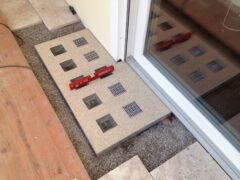 Lichtschachtabdeckung mit mehreren Glassteinen und Entwässerungsrinnen in einem Wohnbereich.