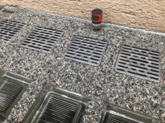 Metallische Lichtschachtabdeckungen mit rutschfester Oberfläche auf Kiesuntergrund.