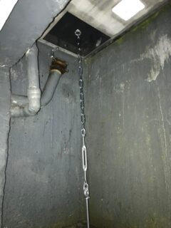 Eine Kette hängt von der Decke in einem Lichtschacht neben einem Rohr.