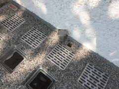 Metallische Lichtschachtabdeckungen mit Rillenmuster auf einem Kiesboden.