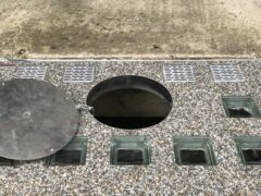 Metallabdeckung über einem Lichtschacht mit einer runden Öffnung und Glassteinen.