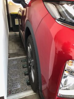 Roter SUV parkt neben einer Lichtschachtabdeckung mit grauem Untergrund und grünen Elementen.