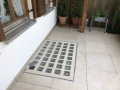 Lichtschachtabdeckung aus Glassteinen auf einem Fliesenboden im Außenbereich.
