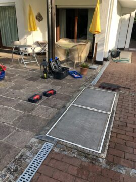 Metallabdeckplatte über einem Entwässerungssystem auf einem gepflasterten Boden.
