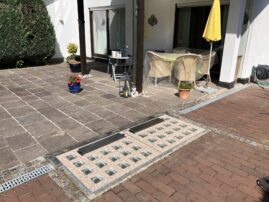 Entwässerungssystem mit Glassteinen und Gitterabdeckung im Außenbereich eines Hauses.